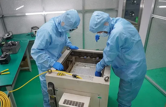 Technicians performing preventive maintenance on industrial laser equipment in a cleanroom